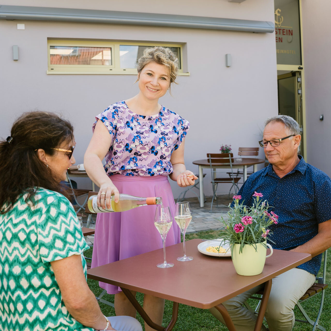 Gastgeberin serviert Sekt im Garten.